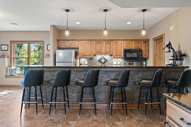 6507 Willow Ct, Waterford, WI 53185 - kitchen featuring freestanding refrigerator, black microwave, a kitchen breakfast bar, decorative backsplash, and hanging light fixtures