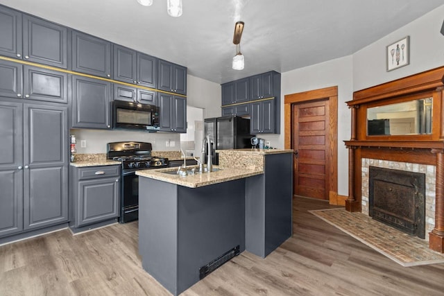 628 Broad St, Menasha, WI 54952 - kitchen with black appliances, light wood-type flooring, a center island with sink, and light stone countertops