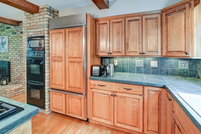 3590 Sabaka Trl, Verona, WI 53593 - kitchen with black appliances, light wood-type flooring, beam ceiling, decorative backsplash, and a wood stove