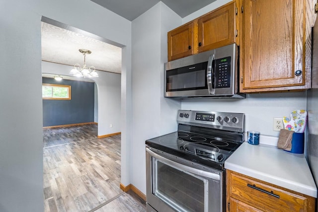 2941 Plover Rd, Wisconsin Rapids, WI 54494 - kitchen with stainless steel appliances, brown cabinets, a chandelier, light wood-style floors, and light countertops