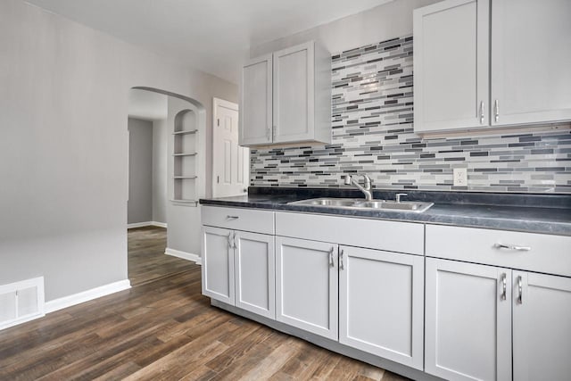 4636 N 19th St, Milwaukee, WI 53209 - kitchen featuring dark countertops, backsplash, dark wood-type flooring, arched walkways, and white cabinetry