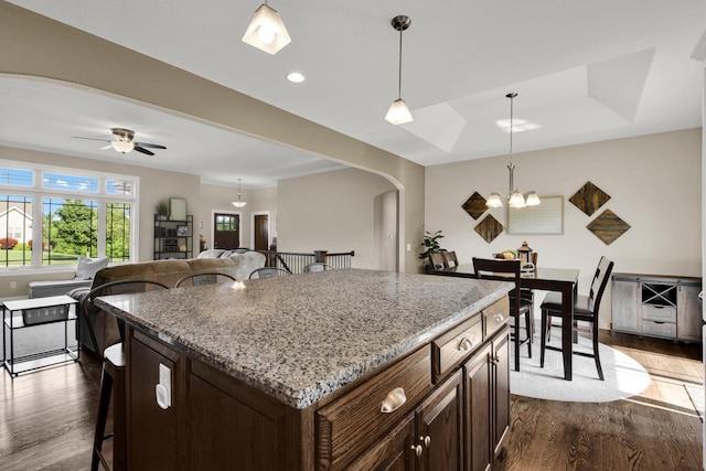 1395 American Eagle Dr, Slinger, WI 53086 - kitchen featuring a breakfast bar, arched walkways, dark wood-type flooring, decorative light fixtures, and light stone countertops