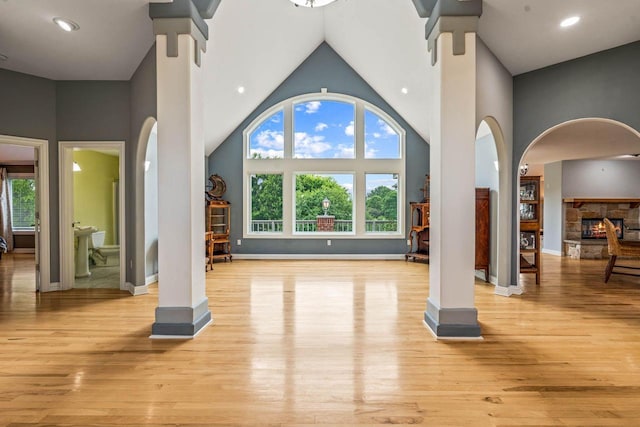 N66W38493 N Woodlake Cir, Oconomowoc, WI 53066 - unfurnished living room featuring wood finished floors, high vaulted ceiling, arched walkways, and a fireplace