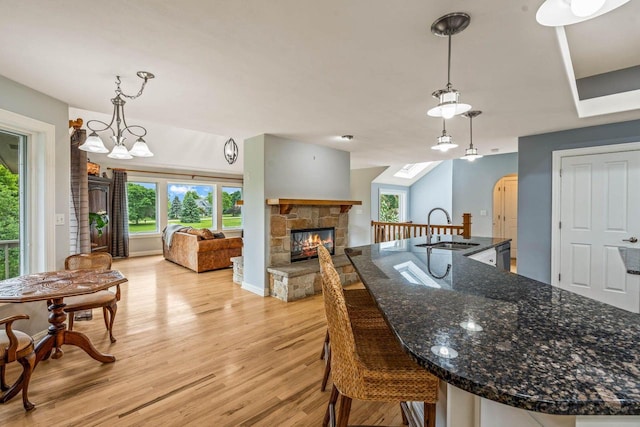 N66W38493 N Woodlake Cir, Oconomowoc, WI 53066 - kitchen featuring a stone fireplace, light wood-type flooring, a breakfast bar, dark stone counters, and a large island with sink