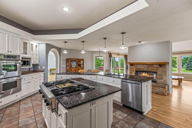 N66W38493 N Woodlake Cir, Oconomowoc, WI 53066 - kitchen with stainless steel appliances, a center island, a stone fireplace, arched walkways, and white cabinetry