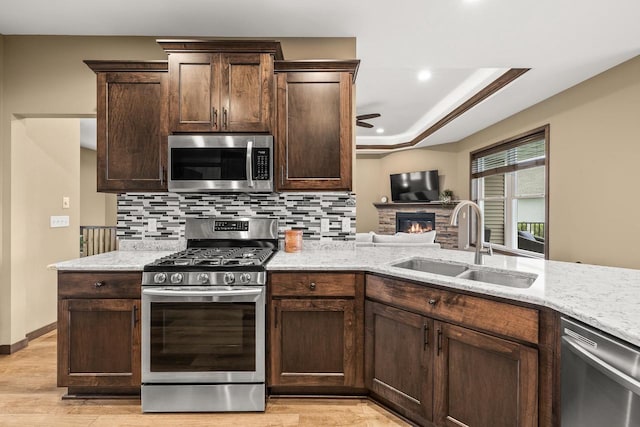 3830 Augusta Ct, Plover, WI 54467 - kitchen featuring appliances with stainless steel finishes, ceiling fan, tasteful backsplash, a stone fireplace, and dark brown cabinetry
