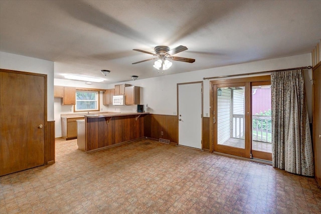 1702 Rae Ln, Madison, WI 53711 - kitchen with white microwave, a peninsula, a wainscoted wall, a breakfast bar, and a ceiling fan
