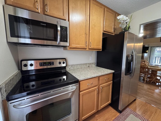 8 Balsam Trl, Wisconsin Dells, WI 53965 - kitchen featuring stainless steel appliances, light wood finished floors, light stone counters, and a textured ceiling