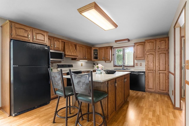 6352 Black Wolf Point Ln, Oshkosh, WI 54902 - kitchen with black appliances, light wood-type flooring, light countertops, brown cabinets, and premium range hood