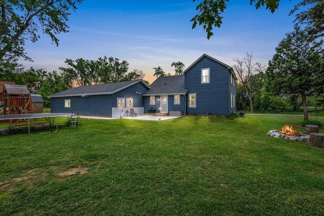 N6965 Thede Rd, Black Creek, WI 54106 - back of house at dusk featuring a trampoline, an outdoor fire pit, a patio area, a yard, and a shingled roof