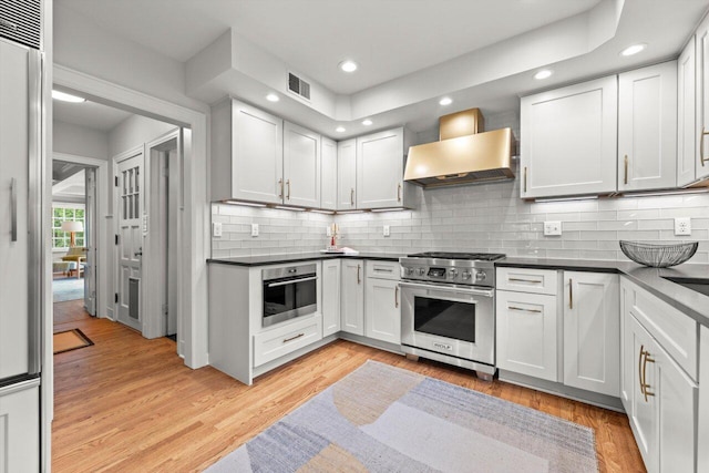 6123 N Berkeley Blvd, Whitefish Bay, WI 53217 - kitchen featuring stainless steel appliances, wall chimney exhaust hood, dark countertops, light wood-style flooring, and recessed lighting
