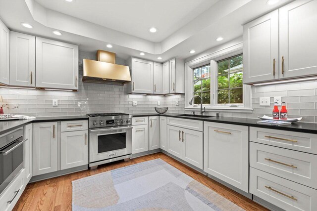 6123 N Berkeley Blvd, Whitefish Bay, WI 53217 - kitchen featuring appliances with stainless steel finishes, wall chimney exhaust hood, recessed lighting, dark countertops, and light wood-style flooring