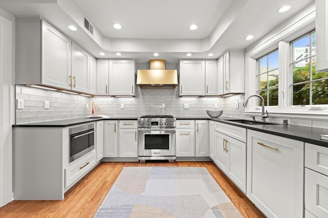 6123 N Berkeley Blvd, Whitefish Bay, WI 53217 - kitchen featuring stainless steel appliances, wall chimney exhaust hood, dark countertops, light wood-type flooring, and recessed lighting