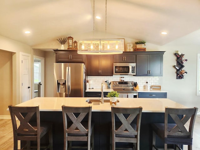104 Mark Ct, Eden, WI 53019 - kitchen with stainless steel appliances, vaulted ceiling, decorative backsplash, light countertops, and a center island with sink