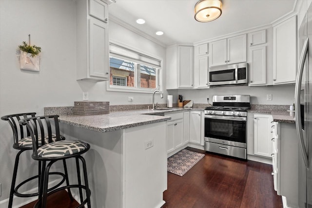 150 E Fairmount Ave, Whitefish Bay, WI 53217 - kitchen featuring appliances with stainless steel finishes, a peninsula, dark wood-style flooring, white cabinets, and a breakfast bar