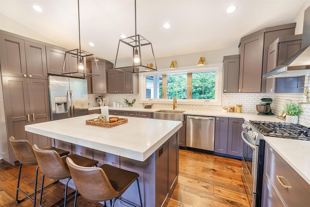 3717 White Pine Dr, Janesville, WI 53545 - kitchen featuring appliances with stainless steel finishes, wall chimney range hood, a breakfast bar area, light wood finished floors, and tasteful backsplash