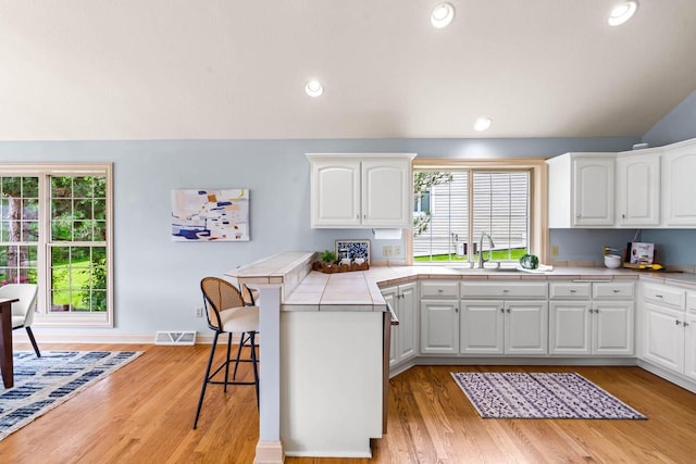 N53W16527 Whitetail Run, Menomonee Falls, WI 53051 - kitchen with tile countertops, a breakfast bar area, healthy amount of natural light, vaulted ceiling, and light wood-style flooring