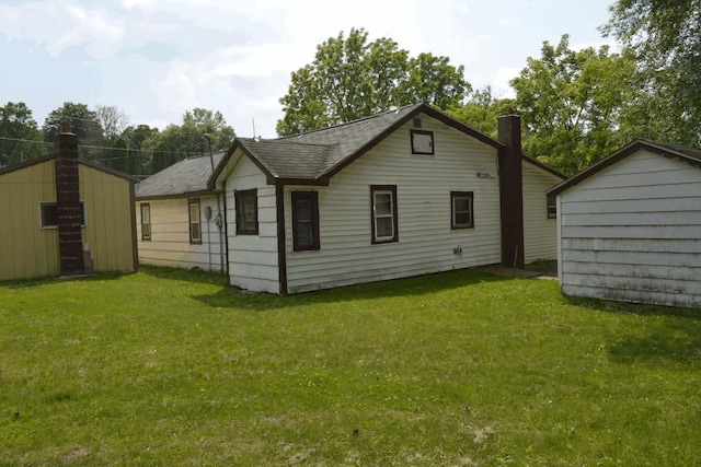 653 Grant St, Wonewoc, WI 53968 - back of house featuring a lawn, a chimney, roof with shingles, and an outbuilding
