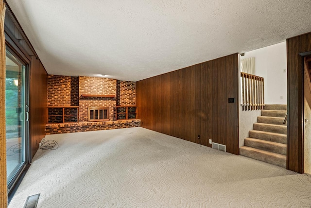 5325 Linden Cir, Racine, WI 53406 - unfurnished living room with carpet, a brick fireplace, wooden walls, stairs, and a textured ceiling