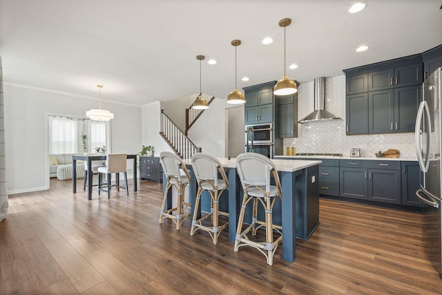 7949 W Oakwood Way, Franklin, WI 53132 - kitchen featuring wall chimney range hood, appliances with stainless steel finishes, light countertops, decorative backsplash, and a center island