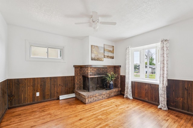 136 Oak St, Brillion, WI 54110 - unfurnished living room with wood finished floors, a baseboard radiator, a wainscoted wall, wood walls, and ceiling fan