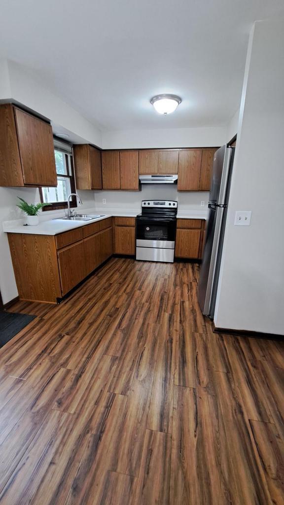 752 Imperial Ct Unit 754, West Bend, WI 53095 - kitchen featuring stainless steel appliances, under cabinet range hood, dark wood-style flooring, light countertops, and brown cabinets