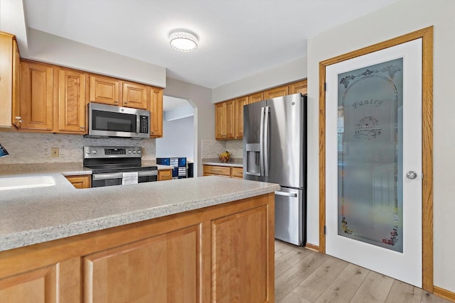 W163N10515 Ridgeview Ln, Germantown, WI 53022 - kitchen featuring stainless steel appliances, light countertops, light wood finished floors, decorative backsplash, and a peninsula