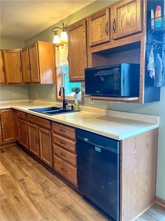 608 3rd St, Cameron, WI 54822 - kitchen with black appliances, light wood-style flooring, a textured ceiling, light countertops, and brown cabinets