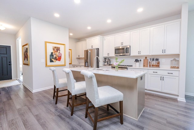 310 Paradise Ct, Hartland, WI 53029 - kitchen featuring stainless steel appliances, an island with sink, a kitchen bar, light countertops, and white cabinets