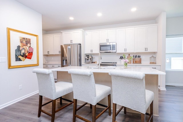 310 Paradise Ct, Hartland, WI 53029 - kitchen with appliances with stainless steel finishes, a center island with sink, a kitchen breakfast bar, light countertops, and white cabinetry