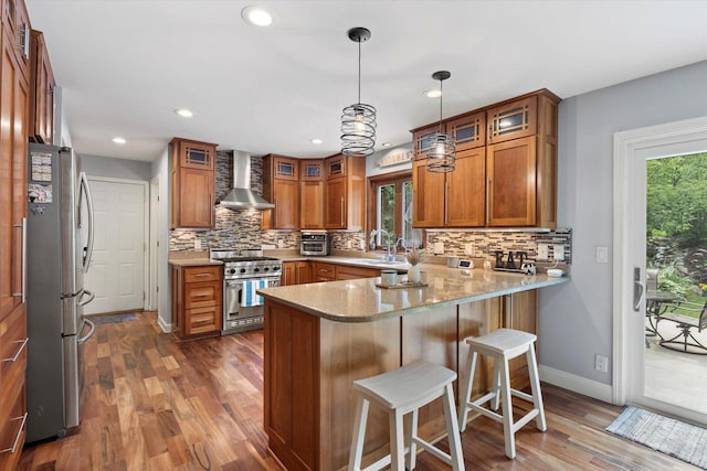 N80W32229 Northbrook Ct, Hartland, WI 53029 - kitchen with appliances with stainless steel finishes, wall chimney exhaust hood, a peninsula, brown cabinets, and tasteful backsplash
