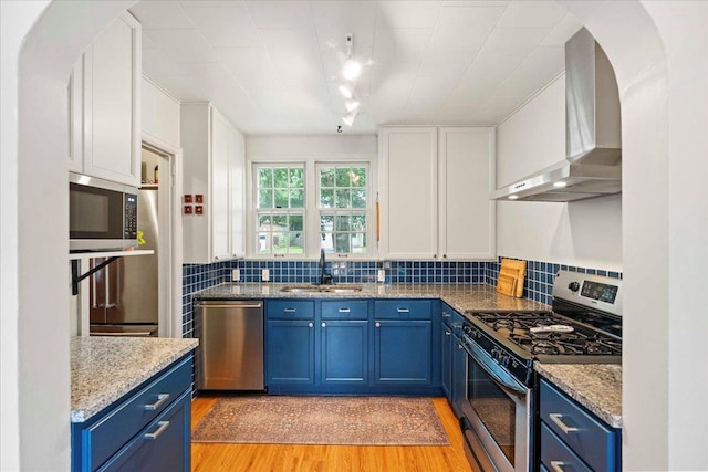 4705 Gordon Ave, Monona, WI 53716 - kitchen with stainless steel appliances, blue cabinets, wall chimney exhaust hood, white cabinetry, and light wood finished floors