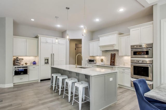 9335 223rd Ave, Salem, WI 53168 - kitchen with decorative backsplash, stainless steel double oven, a kitchen island with sink, white cabinetry, and light wood-type flooring