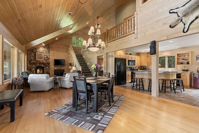 4721 Lake Of The Woods Rd, Sturgeon Bay, WI 54235 - dining room with high vaulted ceiling, a stone fireplace, stairs, a chandelier, and light wood-style flooring