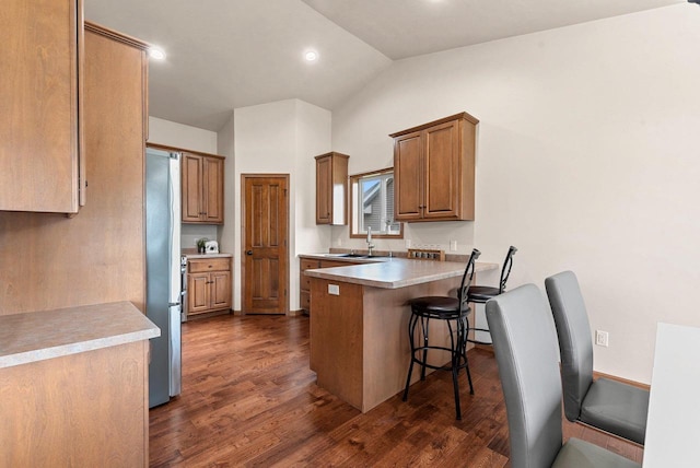 4835 Isabella Cir, Hobart, WI 54155 - kitchen featuring vaulted ceiling, a peninsula, dark wood-type flooring, a breakfast bar, and brown cabinetry