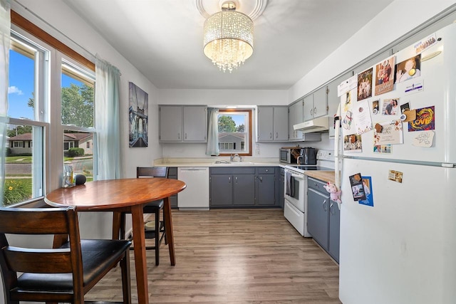 605 E 10th St, Fond Du Lac, WI 54935 - kitchen with white appliances, gray cabinetry, under cabinet range hood, a chandelier, and light wood finished floors