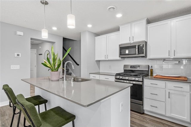7243 Fall Dr, Hugo, MN 55038 - kitchen featuring appliances with stainless steel finishes, wood finished floors, backsplash, a breakfast bar, and white cabinetry