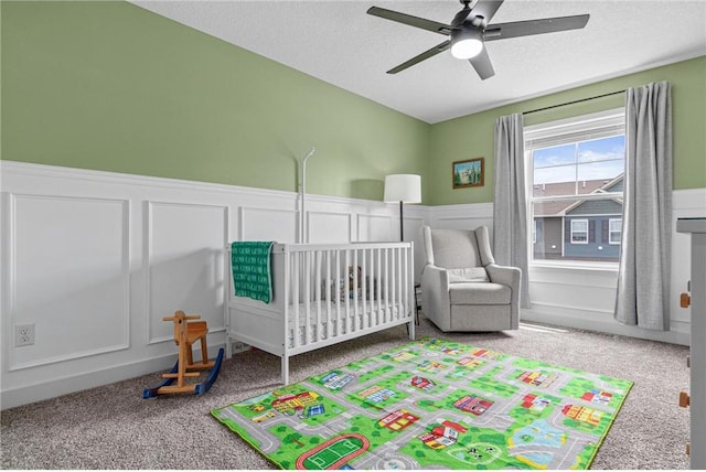 7243 Fall Dr, Hugo, MN 55038 - carpeted bedroom with a nursery area, a wainscoted wall, a decorative wall, a textured ceiling, and a ceiling fan