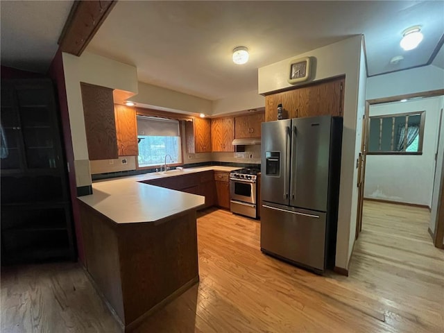 514 S Robert St, Grantsburg, WI 54840 - kitchen with appliances with stainless steel finishes, a peninsula, light wood finished floors, brown cabinetry, and under cabinet range hood