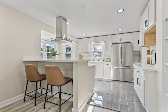 3700 S 21st St, Milwaukee, WI 53221 - kitchen with freestanding refrigerator, island exhaust hood, a breakfast bar area, light countertops, and backsplash