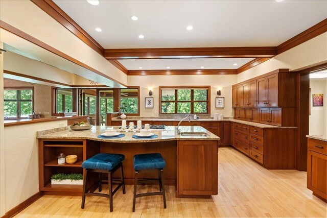 5870 Persimmon Dr, Fitchburg, WI 53711 - kitchen featuring brown cabinetry, light wood-style flooring, light stone countertops, a breakfast bar, and ornamental molding
