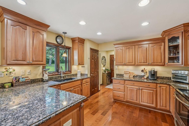 S46W22428 Tansdale Rd, Waukesha, WI 53189 - kitchen featuring electric range, dark stone countertops, glass insert cabinets, light wood-style floors, and pendant lighting