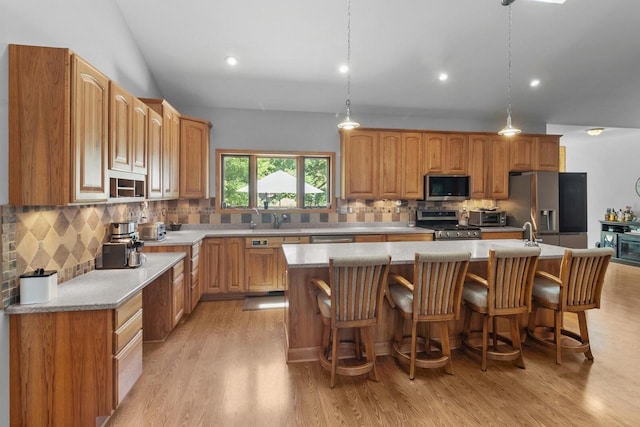 1201 Lance Dr, Twin Lakes, WI 53181 - kitchen featuring appliances with stainless steel finishes, light wood-style flooring, light countertops, decorative backsplash, and an island with sink
