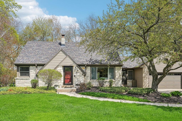 2040 San Fernando Dr, Elm Grove, WI 53122 - tudor house featuring stone siding, a front yard, an attached garage, a chimney, and roof with shingles