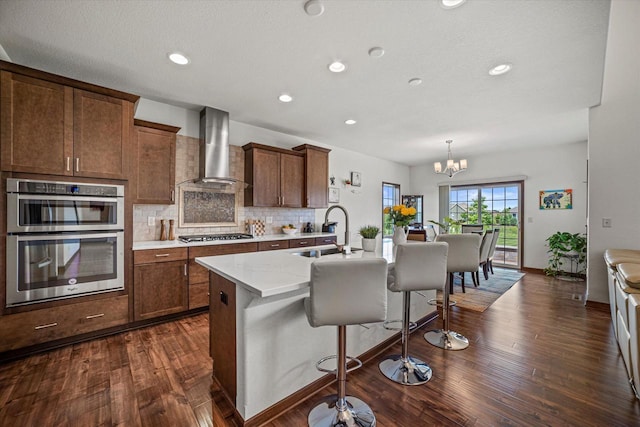 10870 N Spartan Cir, Mequon, WI 53097 - kitchen with wall chimney range hood, dark wood finished floors, a center island with sink, a breakfast bar area, and backsplash