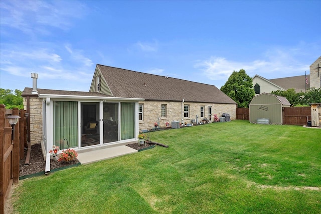 20903 W Main St, Lannon, WI 53046 - rear view of property featuring stone siding, a storage unit, a fenced backyard, roof with shingles, and a sunroom