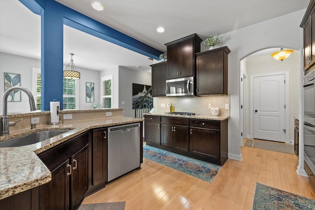 8061 S River Ln, Franklin, WI 53132 - kitchen featuring stainless steel appliances, decorative backsplash, dark brown cabinets, light stone countertops, and arched walkways
