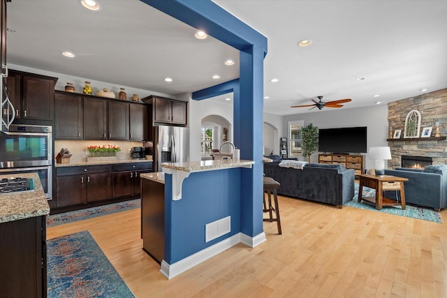 8061 S River Ln, Franklin, WI 53132 - kitchen with appliances with stainless steel finishes, arched walkways, a kitchen breakfast bar, dark brown cabinets, and recessed lighting