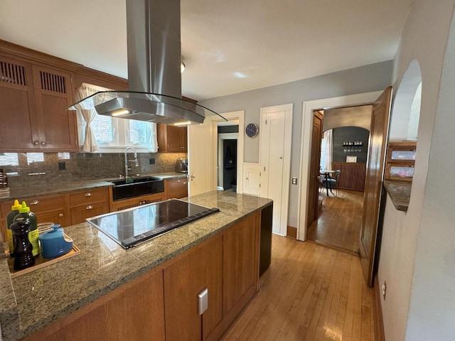 6309 W Mckinley Ave, Wauwatosa, WI 53213 - kitchen featuring island exhaust hood, black electric stovetop, brown cabinetry, light wood-style flooring, and decorative backsplash