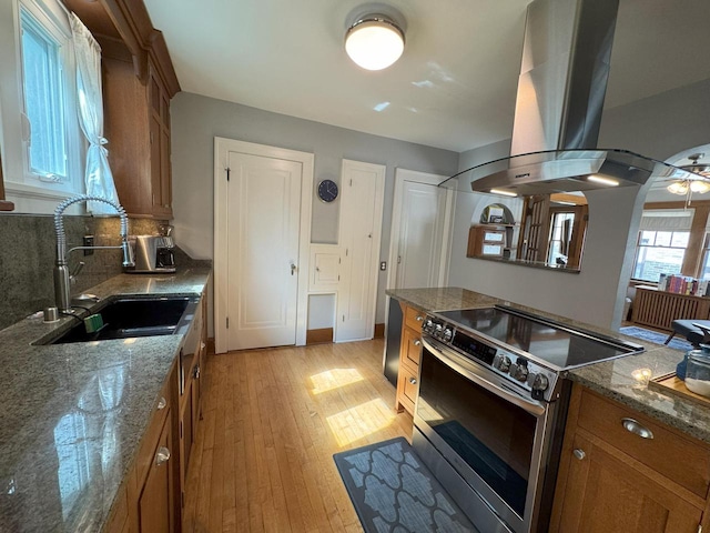 6309 W Mckinley Ave, Wauwatosa, WI 53213 - kitchen with stainless steel electric range oven, brown cabinets, island range hood, light wood finished floors, and decorative backsplash